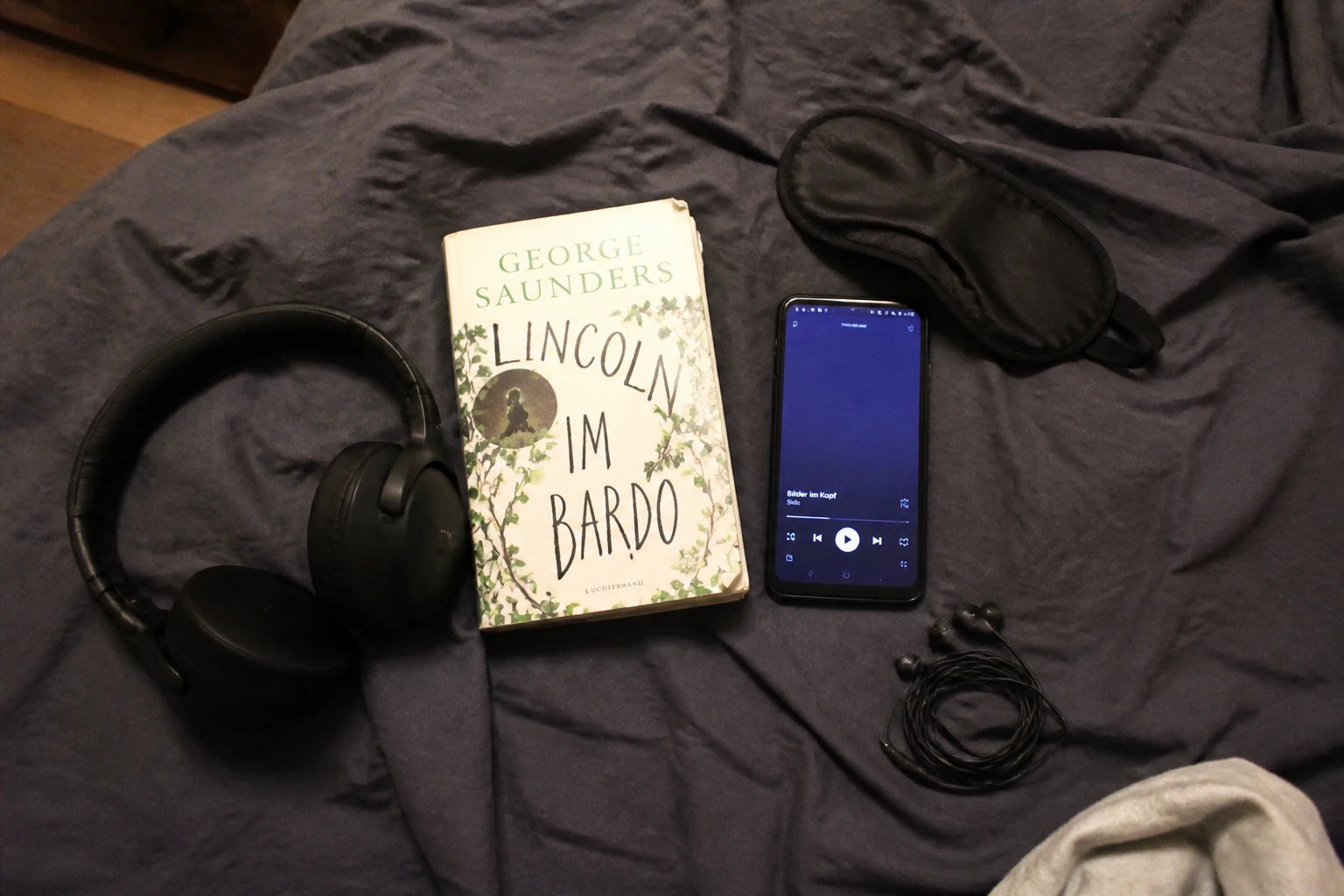Selbst fotografiertes Test-Setup: Kopfhörer, Handy, Buch und Schlafmaske auf dem Bett