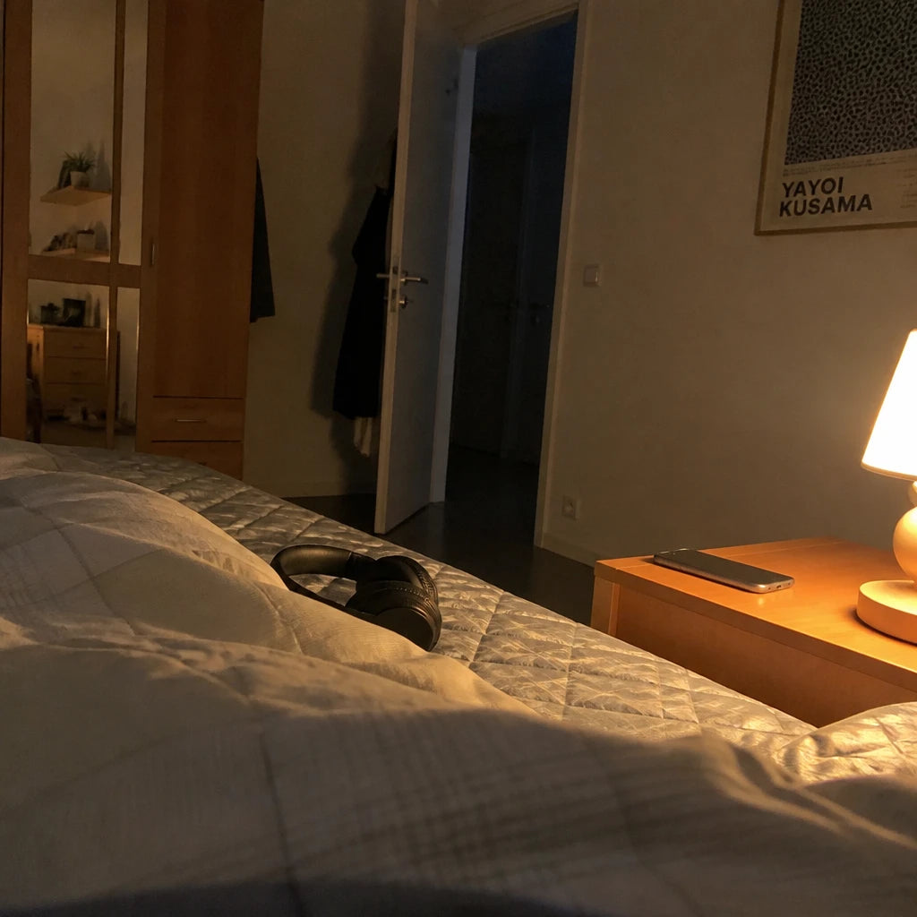 Abend B aus deiner Sicht: Handy umgedreht auf dem Nachttisch, Kopfhörer auf, warmes Lampenlicht