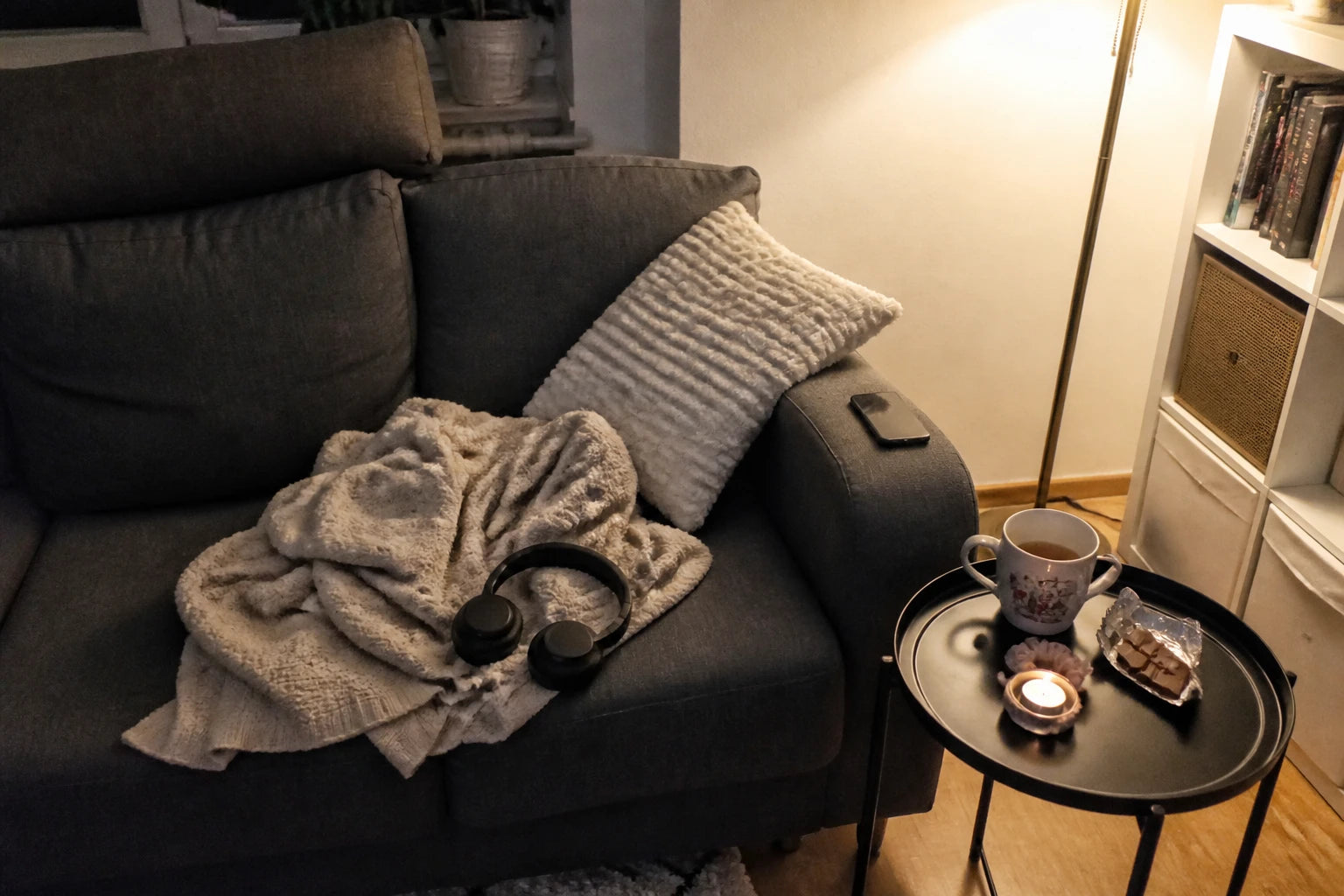 Handy-Schnappschuss meiner Sofa-Ecke am Abend: Kopfhörer auf der Decke, Tee und Kerze auf dem Beistelltisch, Handy umgedreht auf der Armlehne